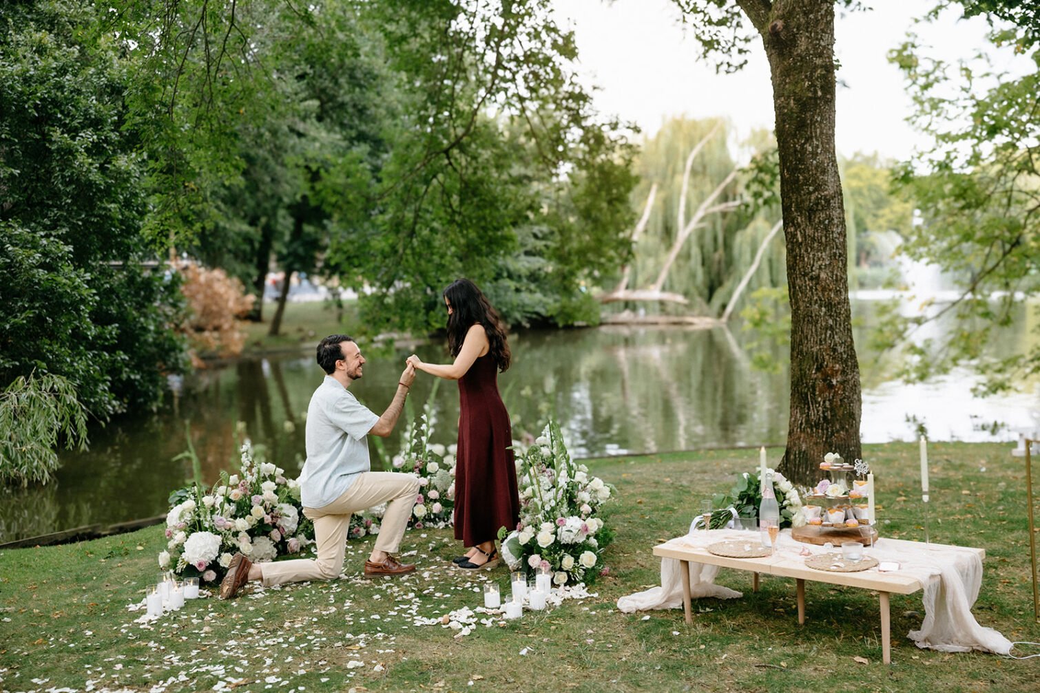 Proposal flower decoration with white and pink flowers, candles and a picnic table beside a park pond