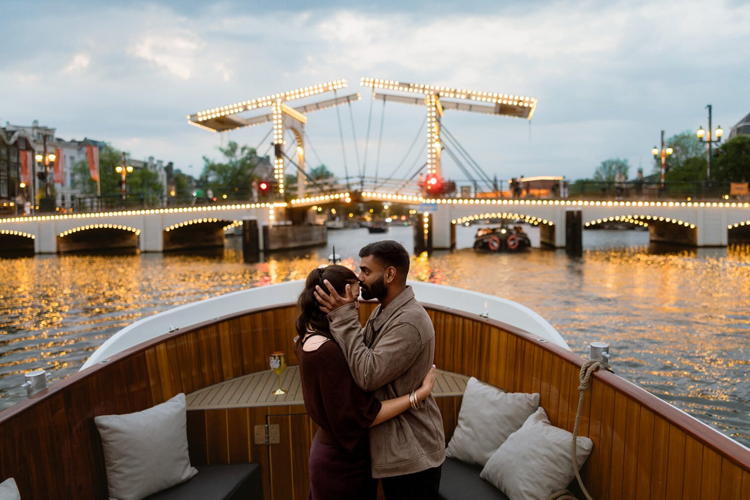 Couple embracing on an Amsterdam canal boat with an illuminated drawbridge in the background