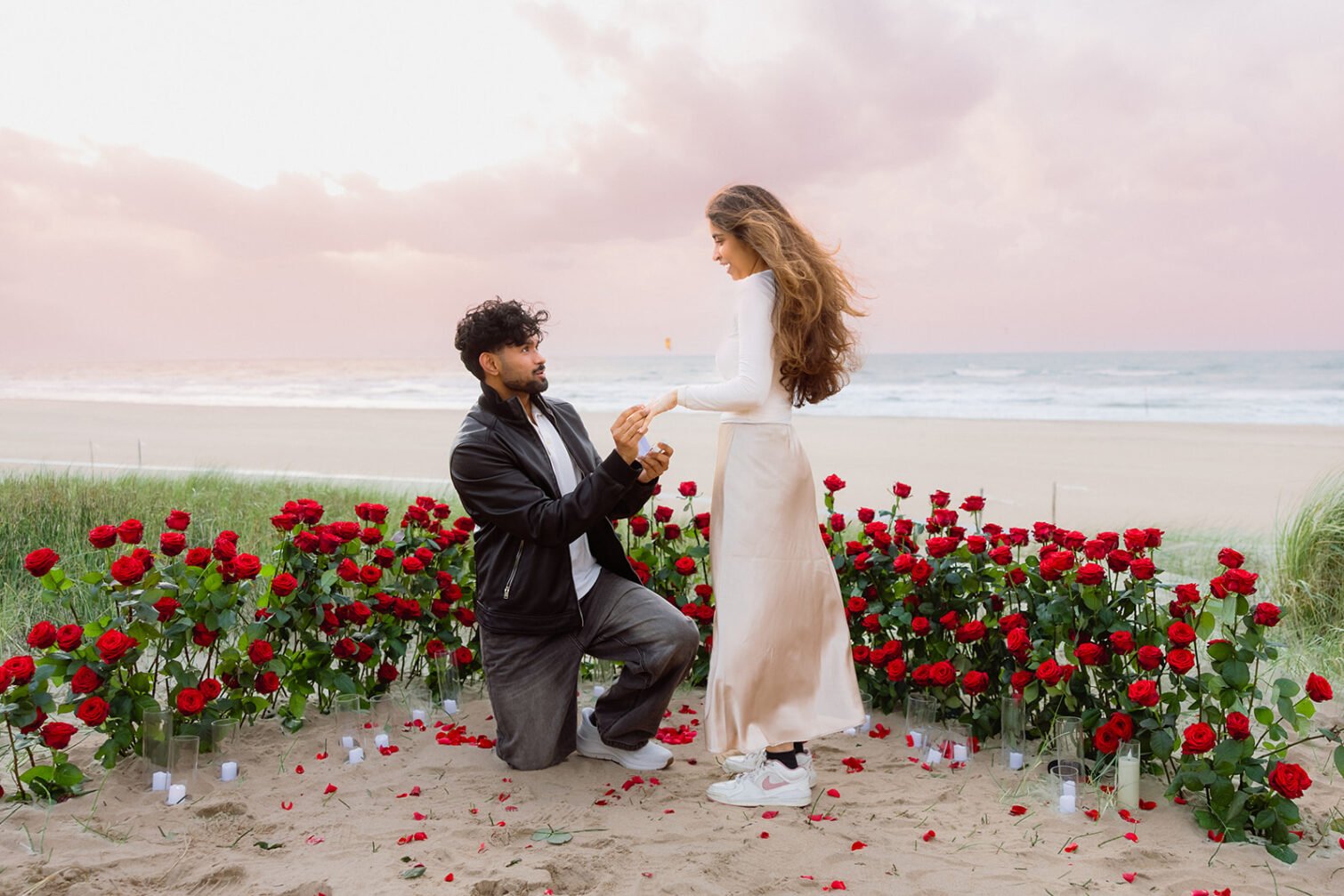 Beach proposal with red rose flower decoration, rose petals and candles beside the sea