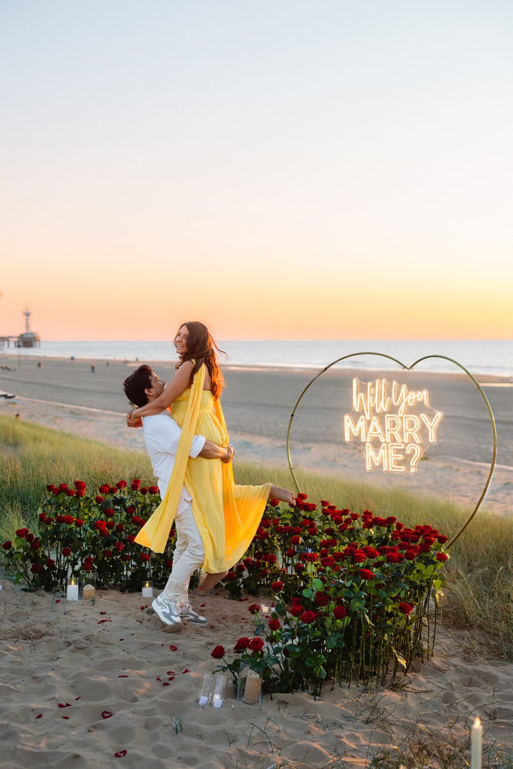 Proposal flower decoration with red roses, candles and illuminated Marry Me sign on the beach