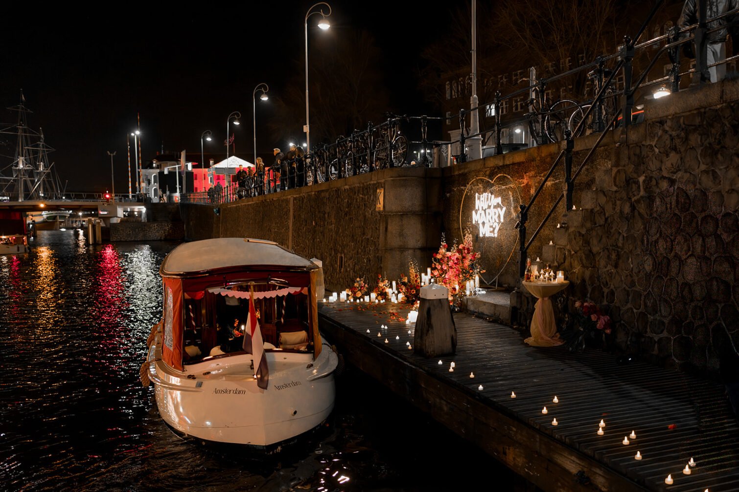 Proposal decoration Amsterdam with flowers, candles and illuminated Marry Me sign beside a canal boat