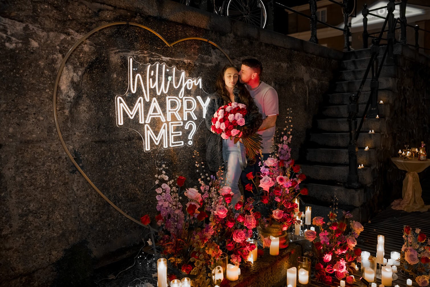 Proposal decoration with colorful flowers, candles and a heart-shaped illuminated Marry Me sign